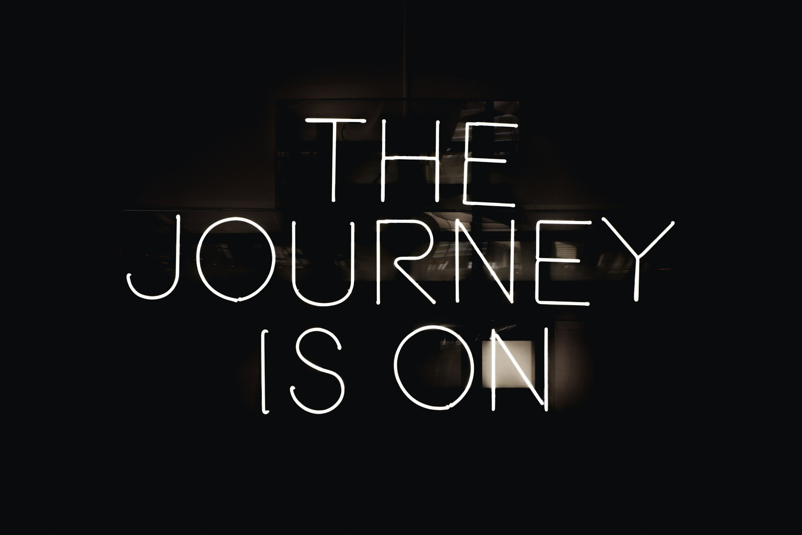 A black background showing a window at night with neon text overlaying it that reads, "The journey is on."